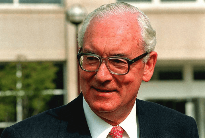 A man in glasses and suit with white hair.